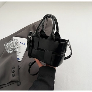 Detail of glossy black woven bucket bag with smooth leather handles and silver hardware