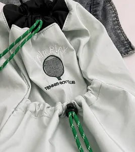 Close-up of embroidered tennis racket logo and Fair Play text on light green backpack