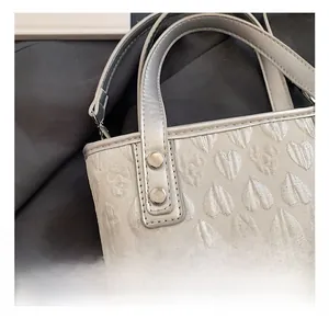Close-up of silver heart-embossed handbag showing metal rivets and premium texture
