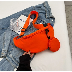 Close-up of bright orange canvas sling bag with small round pouch on denim background