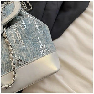 Detailed close-up of light blue denim bucket bag with silver sequins and chain strap