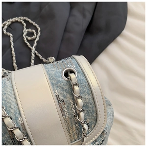 Detail of light blue sequin bucket bag with white leather trim and metal chain strap
