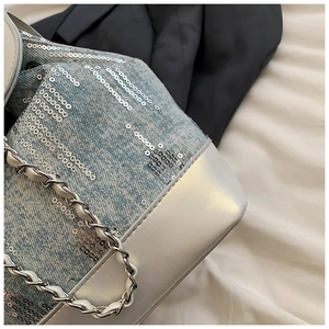 Close-up of light blue denim bucket bag featuring silver sequins and metal chain strap