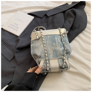 Close-up of light blue denim bucket bag with silver sequins on white fabric background