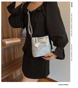 Close-up of metallic silver bucket bag featuring a decorative bow and slim shoulder strap