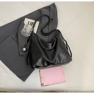 Detailed flat lay of black crocodile embossed tote bag with adjustable strap and metal tag