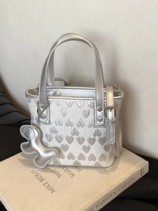 Silver heart-patterned handbag with bear charm and adjustable strap on a book base
