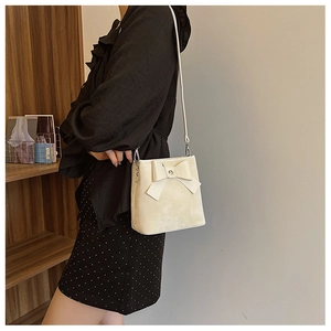 Detail of cream white bucket bag with large bow and leather strap worn by a model