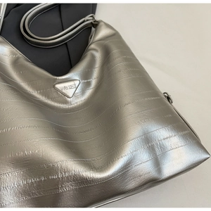 Macro shot of silver metallic tote bag featuring pleated texture and triangular metal logo