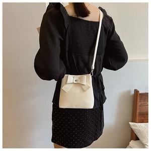 Crossbody bucket bag with bow detail shown on model against minimalist home background