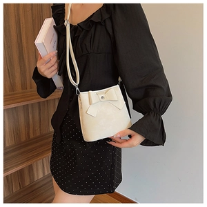 Detailed view of white bucket bag featuring a large leather bow and slim shoulder strap