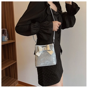 Close-up of a metallic silver bucket bag featuring a large 3D bow and slim shoulder strap