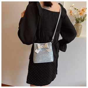 Detail showing metallic silver bucket bag with a large bow and thin crossbody strap