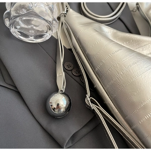 Detail of silver metallic tote bag with horizontal pleated texture and round metal charm