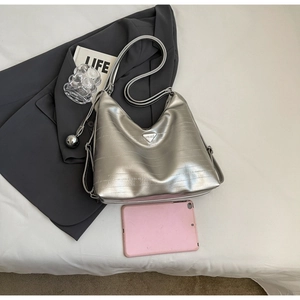 Silver metallic tote bag with triangular logo and spherical pendant on a grey blazer