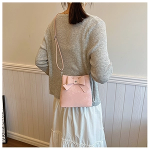 Detail of a sweet pink crossbody bucket bag featuring a large decorative bow and leather texture