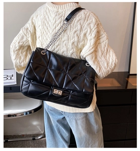 Detail of black quilted leather shoulder bag featuring silver chain strap and metal turn-lock