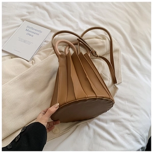 Détail du sac seau plissé marron avec poignée ronde posé sur une literie blanche