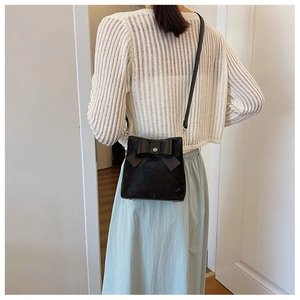 Detail of a black crossbody bag with a large bow worn by a model in a stylish indoor setting