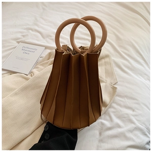Détail du sac seau plissé marron chaud avec poignées circulaires sur literie blanche