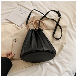 Détail d'un sac seau plissé noir avec poignées roses circulaires et bandoulière amovible