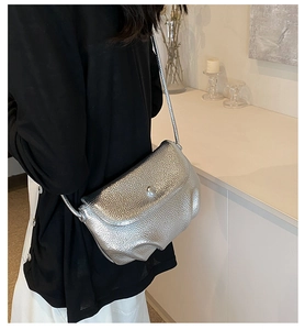 Silver metallic crossbody bag with textured leather and metal buckle worn by a model