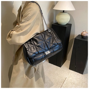 Detail of black quilted shoulder bag featuring silver chain strap and metal twist lock
