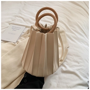 Détail du sac seau plissé beige avec anse ronde aspect bois sur fond minimaliste moderne