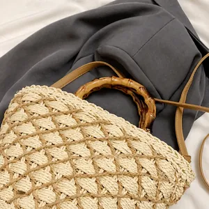Detail of straw woven bag featuring natural bamboo handles and slim leather shoulder strap