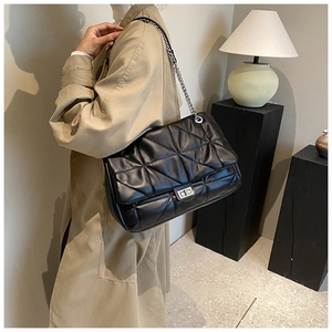 Detailed close-up of silver metal chain strap and twist lock on black quilted shoulder bag