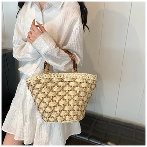 Detailed view of woven straw tote bag featuring natural bamboo handle and gold hardware