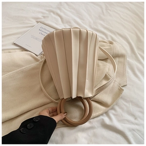 Détail d'un sac plissé crème avec poignées rondes en bois sur un tissu texturé doux