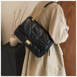 Detail of black quilted shoulder bag with gold chain strap and metallic turn-lock closure