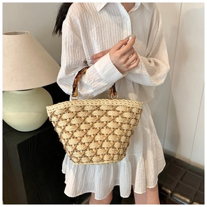 Close-up of hand-woven straw bag featuring retro bamboo handles and gold hardware details