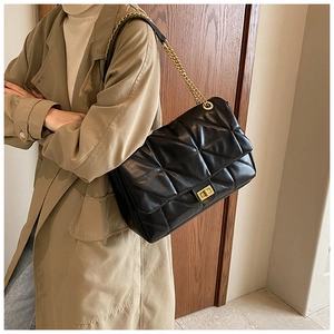 Detail of black quilted leather shoulder bag with gold chain strap and turn-lock closure