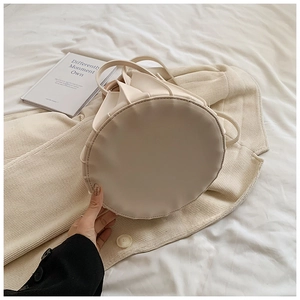 Détail macro du sac seau crème avec plis élégants et anse fine sur un blazer beige