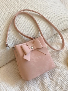 Pink faux suede bucket bag with a large bow and thin shoulder strap on soft background