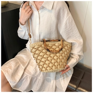 Detail of woven straw handbag with bamboo handles and adjustable brown leather shoulder strap