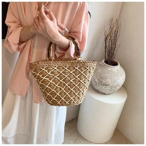 Detail of hand-woven straw bag featuring bamboo handle and white mesh overlay decor