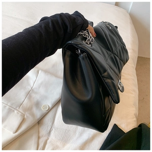 Detail of black quilted shoulder bag with silver chain strap and metal turn-lock