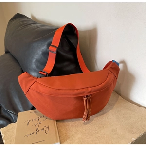 Détail du sac banane en toile orange avec tirettes tressées et bandoulière sur surface en pierre
