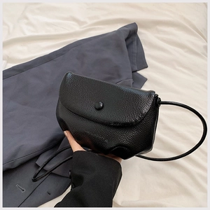Close-up detail of black litchi pattern leather texture on a minimalist crossbody bag