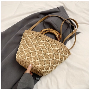 Detail of woven straw bag showing bamboo handles and faux leather strap on grey blazer