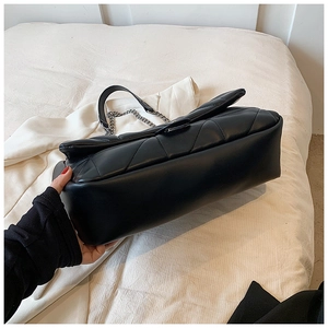 Close-up of black quilted shoulder bag featuring silver chain and spacious bottom detail