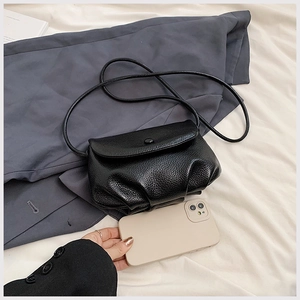 Detailed view of mini black lychee texture crossbody bag next to a smartphone for size