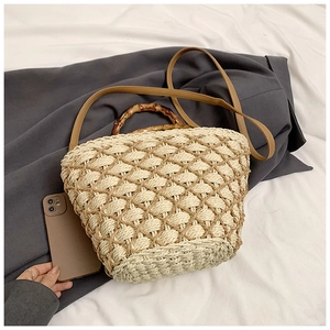 Detail of woven straw handbag featuring bamboo handle and hollow mesh texture with smartphone