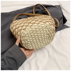 Detail of woven straw bag showing two-tone fiber texture and brown leather strap