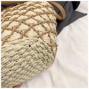 Close-up of woven straw bag showing dual-tone diamond pattern and leather strap detail