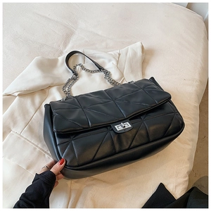 Detail of black quilted chain bag with silver twist lock on light blazer fabric