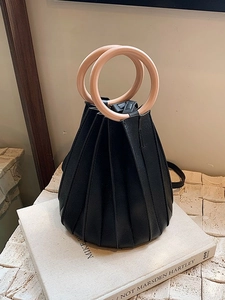 Sac seau plissé noir avec poignées rondes posé sur une pile de livres déco